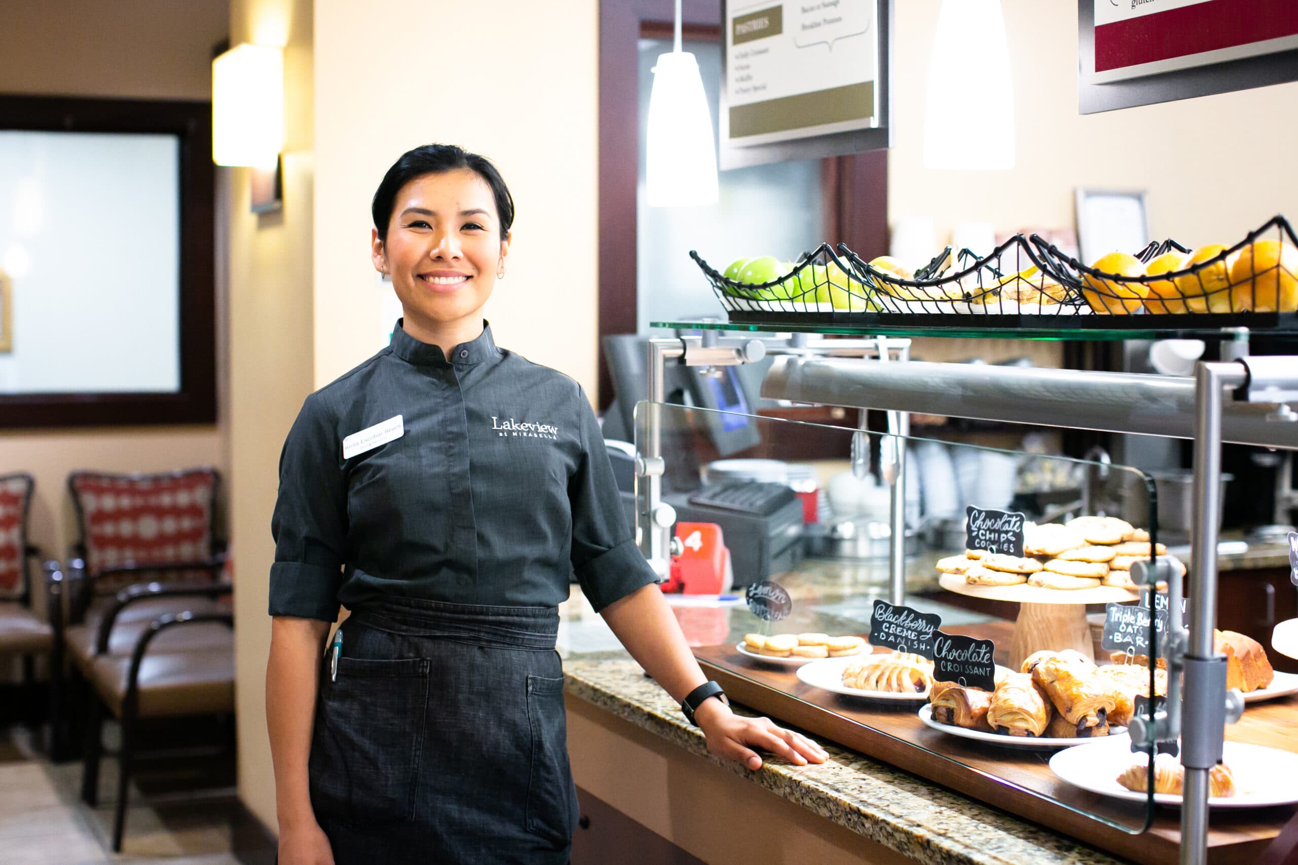 A food service employee smiles next to a case of pastries.