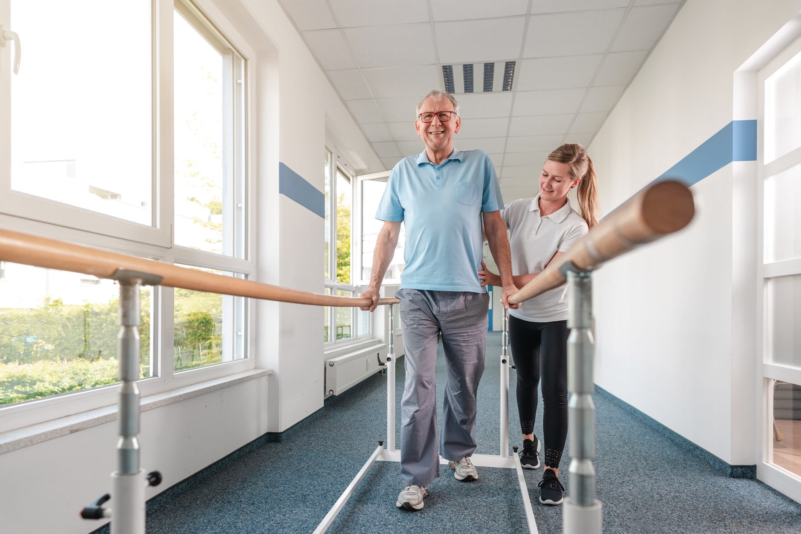A patient walks down the hallway with the help of a walking device and a physical therapist.