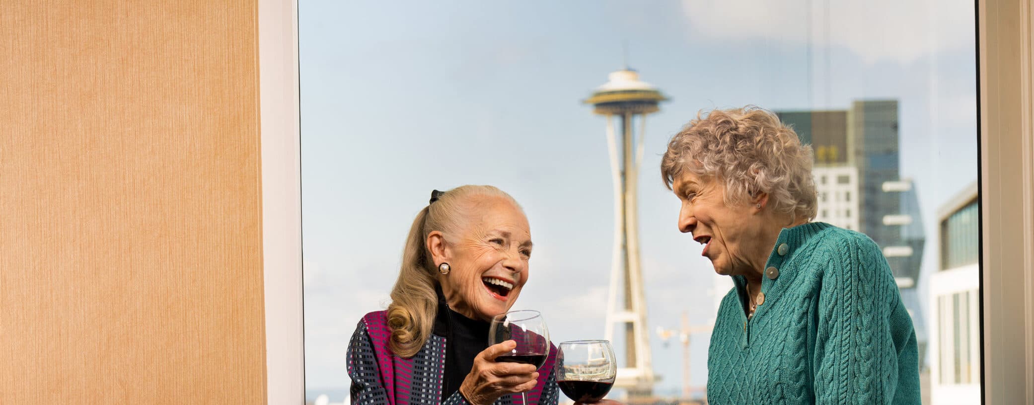 Two older women laugh and talk with glasses of wine at Mirabella Seattle.