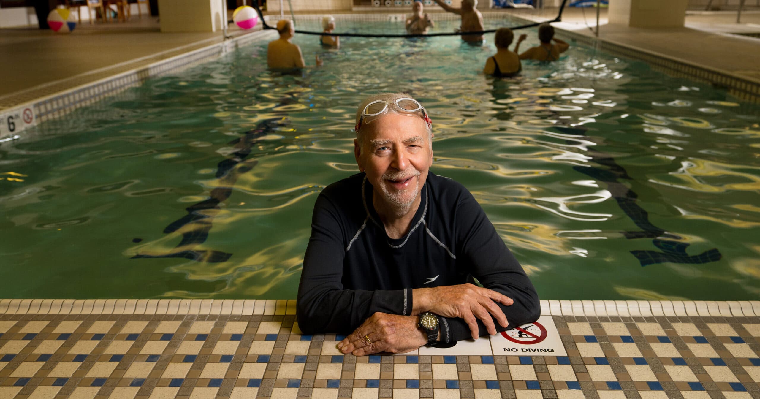 An older man smiling while resting on the side of the pool.